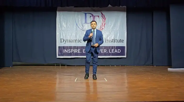 A participant in a suit speaking from the stage of an auditorium at Dynamic Training Institute