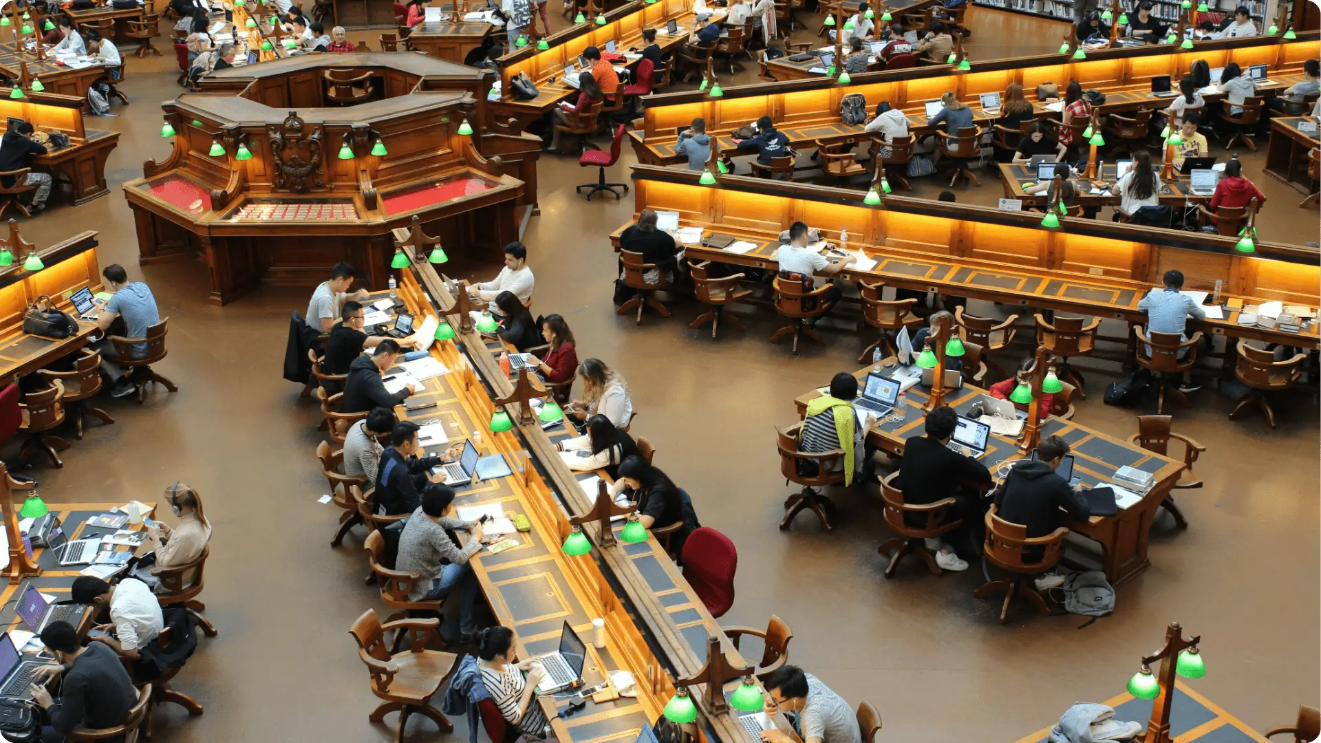 Students studying at long wooden tables in a large library
