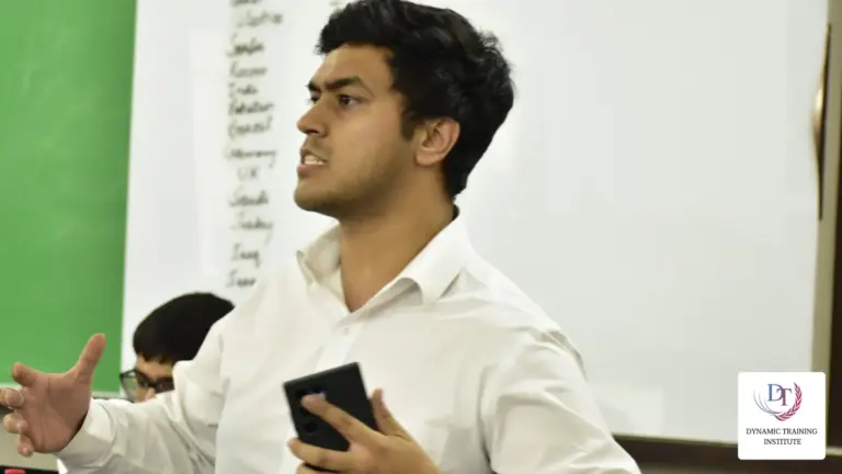 A young man speaking with energy and gesturing in front of a whiteboard