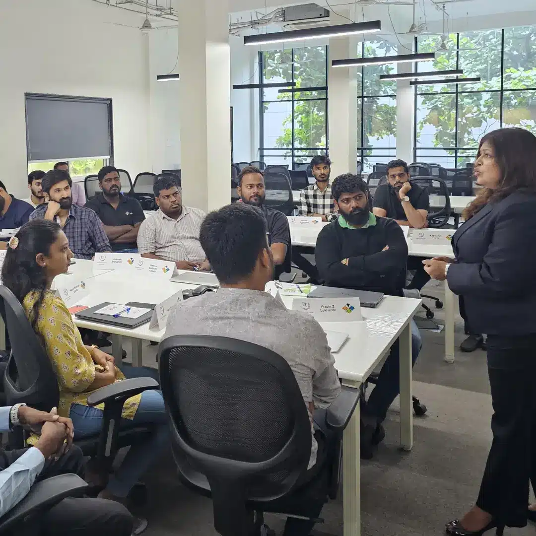 A woman trainer standing and speaking to professionals seated at tables in an office training room