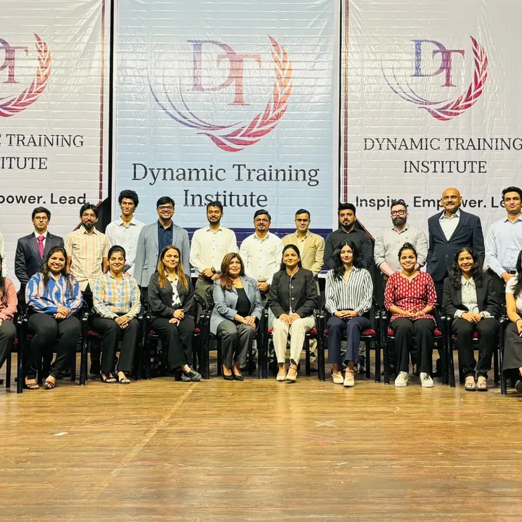 Group photo of a training batch in front of Dynamic Training Institute banners reading “Inspire. Empower. Lead.”
