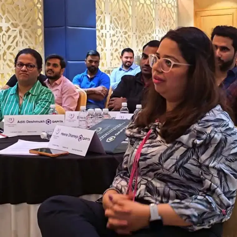 Participants listening at round tables during a training session, a woman in a patterned blouse in front