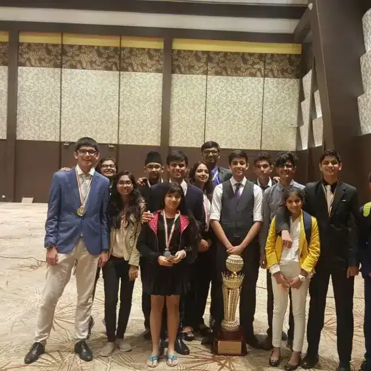 Students in blazers with medals and a trophy, posing as a team in a hotel hall