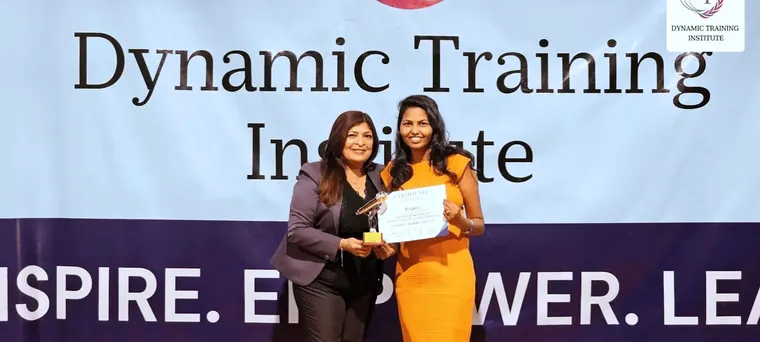 Tina Shah presents a certificate and a trophy to a participant on stage at Dynamic Training Institute