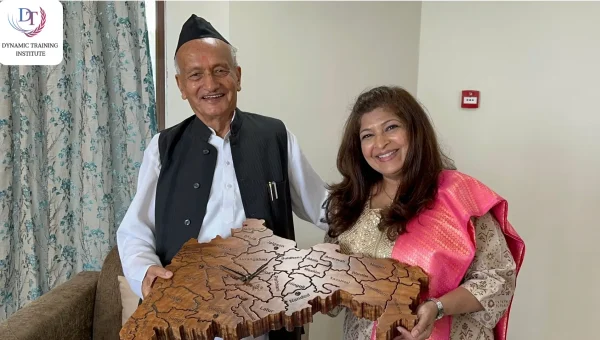 A woman wearing a pink silk stole and an elderly man in a black cap holding a carved wooden map together