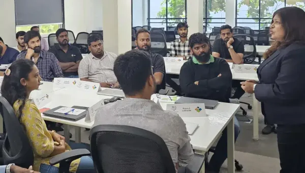 A woman trainer standing and speaking to professionals seated at tables in an office training room