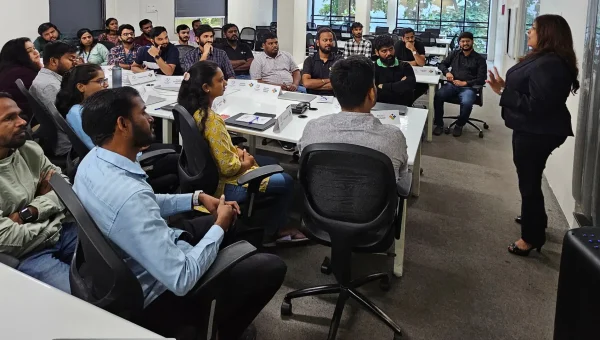 A trainer standing at the front of an office training room, speaking to professionals seated at desks