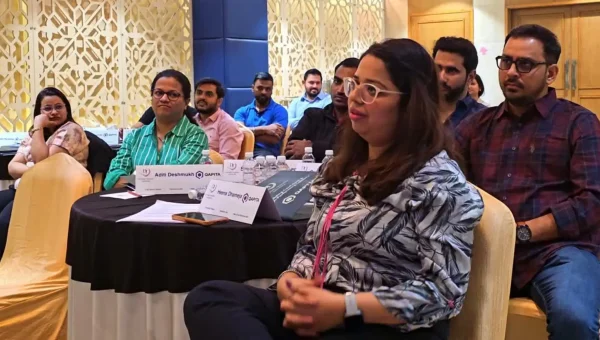 Participants listening at round tables during a training session, a woman in a patterned blouse in front